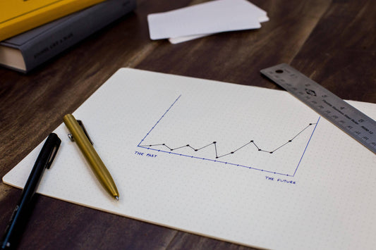 A line graph on a table with a rule, two pens, notecards, and two books